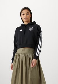 Sudadera negra corta con capucha, diseño de tres franjas blancas de Adidas en las mangas, con logo bordado del fútbol alemán en el pecho.