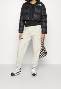 Svart kort puffjacka med en blänkande yta, ihop med krämfärgade joggers. Tillbehör inkluderar en svart och vit rutig väska och sneakers.