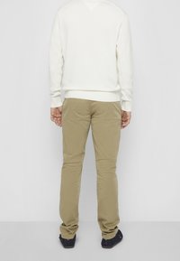 Leichter Creme-Pullover mit geripptem Saum, kombiniert mit khakifarbenen Hosen in geradem Schnitt, beide von hinten vor einfachem Hintergrund gesehen.