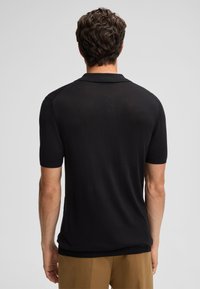 Polo shirt nero a maniche corte con colletto e polsini a coste. Tessuto liscio, design minimal, taglio aderente e spacchi laterali all'orlo.