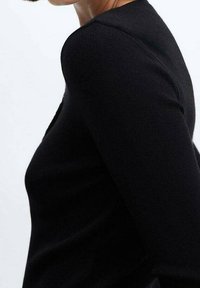 Czarny prążkowany sweter o dopasowanej sylwetce, z okrągłym dekoltem i długimi rękawami. Gładka tekstura z minimalnymi detalami.