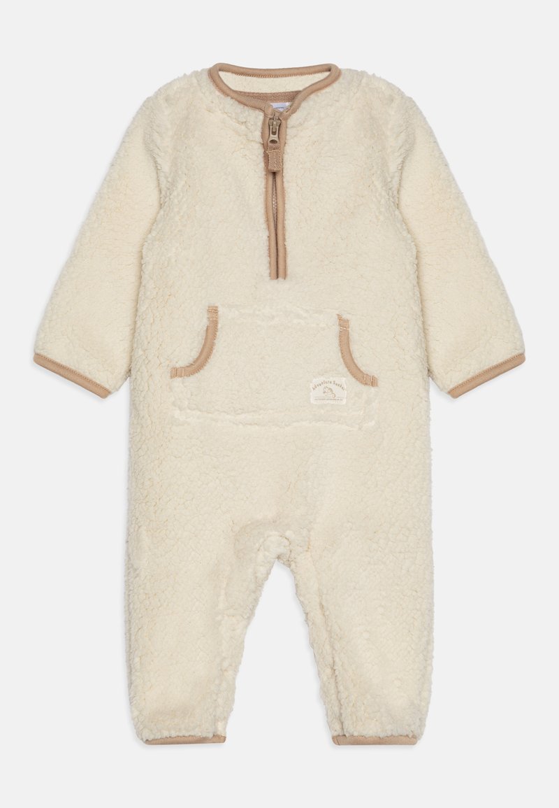 Cremefarbener Fleece-Overall mit langen Ärmeln, Reißverschluss und einer Fronttasche. Mit tanfarbener Rippkante und weichem Material.