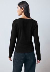 Top negro de manga larga con un escote amplio y textura acanalada. Combinado con vaqueros oscuros de cintura alta que realzan una silueta ajustada.