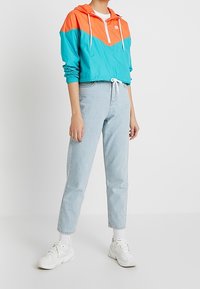 Lättvikts, turkos och orange huppjacka med dragkedja, åtdragen midja och matchande jeans; bärs med vita sneakers och ankelsockor.