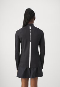 Svart atletisk långärmad tröja med ett vitt vertikalt rand och logotyp på baksidan. Tillverkad av ett mjukt, elastiskt material.
