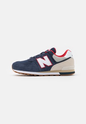 Męski sneakers New Balance w kolorze granatowym, beżowym i czerwonym z białym logo "N" i gumową podeszwą, widoczny z boku na białym tle.