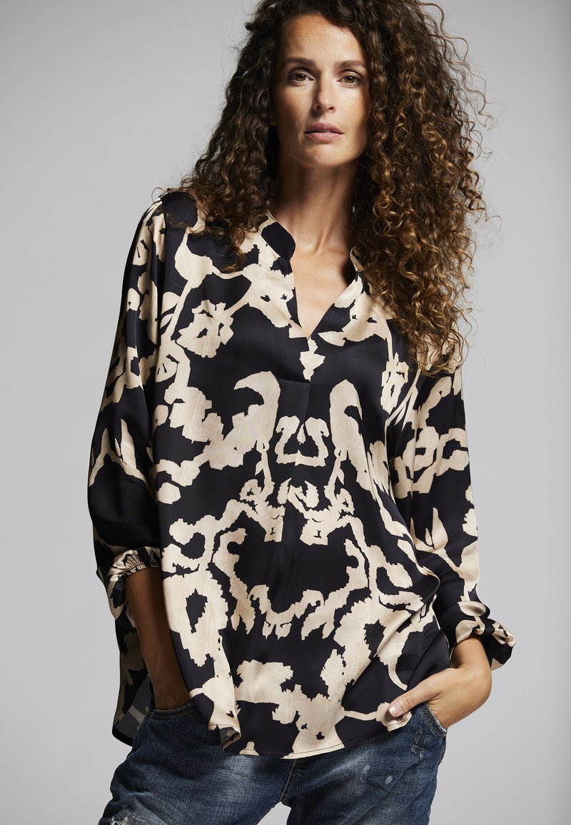 Schwarz-beige gemusterte Bluse mit V-Ausschnitt, legerem Schnitt und langen Ärmeln. Weicher Stoff mit abstrakten Designs und Raffungen an den Manschetten.