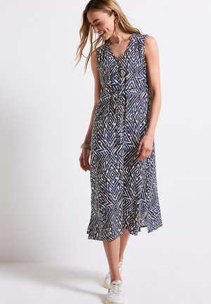 Sleeveless blue and white patterned dress with a V-neck, belted waist, and flared hem. Worn with white sneakers and a bangle bracelet.