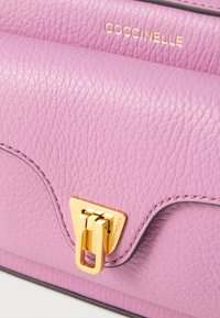 Pink leather handbag with a structured design, featuring a gold hardware clasp and embossed logo. Textured surface with contrasting trim.