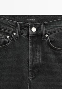 Jeans in denim nero con vita alta. Le caratteristiche includono una chiusura con bottone frontale, due tasche e cuciture visibili. Etichetta del marchio nella parte superiore.
