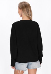 Pulover negru cu o croială lejeră, textură striată și mâneci lungi. Combinate cu blugi scurți, evidențiind un aspect casual și stratificat.