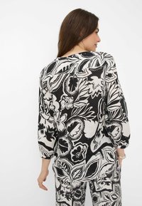 Schwarz-weiß gemusterte Bluse mit langen Ärmeln und lockerer Passform. Der strukturierte Stoff zeigt auffällige Blatt- und Blütendesigns.
