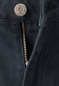 Dunkle Jeanshosen verfügen über einen silbernen Reißverschluss an der Vorderseite mit einem Metallknopfverschluss. Der Stoff hat ein strukturiertes, geripptes Muster.