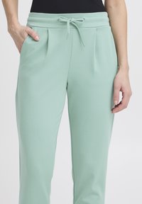 Mintgröna joggers med en dragsko i midjan, veckad framdel och sidofickor. Tillverkade av ett mjukt, slätt material med en avslappnad passform.