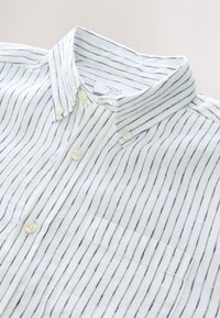 Weißes Hemd mit Knöpfen und navyblauen vertikalen Streifen, mit Kragen, vier Knöpfen und einer Brusttasche, aus strukturiertem Stoff gefertigt.