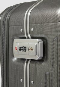 Grijze harde koffer met een gestructureerd oppervlak, zilveren accenten en een combinatiehangslot dat duidelijk zichtbaar aan de voorkant is geplaatst.