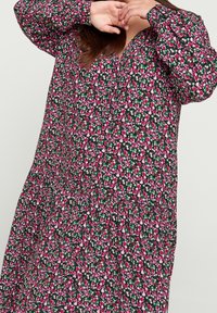 Robe florale avec un fond sombre et des fleurs roses, rouges et blanches, à manches longues, décolleté en V et design de jupe à volants.