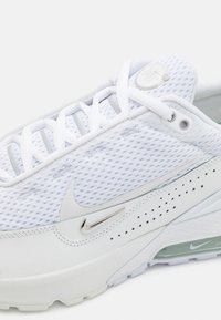Vita Nike Air Max-sneakers med mesh-överdel, vita snören, silverfärgade swoosh-logotyper och synlig luftkudde i sulan.
