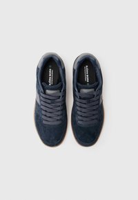 Une paire de baskets en suède bleu marine avec des lacets gris et des semelles en caoutchouc, marquées "Björn Borg," vues de dessus sur un fond blanc.
