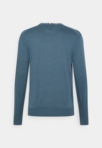 Maglione blu a maniche lunghe con colletto a girocollo a coste. Texture liscia, con un accento triangolare sul collo posteriore e sottili spacchi laterali.