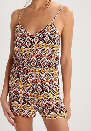 Femme portant une combinaison sans manches avec un motif géométrique coloré en orange, jaune, noir et blanc, avec une taille cintrée et des bretelles fines.