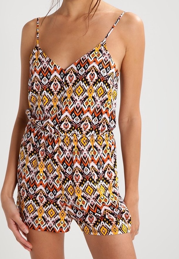 Femme portant une combinaison sans manches avec un motif géométrique coloré en orange, jaune, noir et blanc, avec une taille cintrée et des bretelles fines.