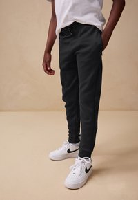 Pantaloni jogger neri con vita elasticizzata e coulisse. Presentano tasche laterali e gambe rastremate, abbinati a sneakers bianche Nike.
