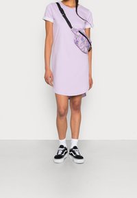 Lilacová oversized tričková šaty s rollovanými bílými rukávy, doplněné multibarevnou ledvinkou a černobílými teniskami.