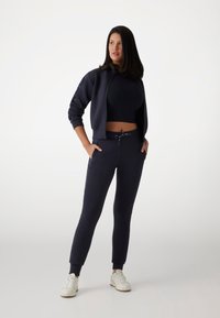 Maritiem trainingspak met een ritsjack en strakke broek met zakken. Geribbelde textuur, broek met trekkoord in de taille en accentstiksels.
