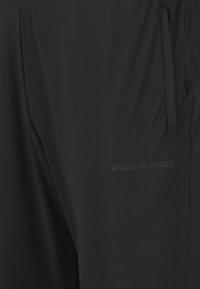 Zwarte sportbroek van gladde stof, met een zijzak en een reliëf "ENDURANCE" logo, voorzien van een lichte, gestroomlijnde uitstraling.
