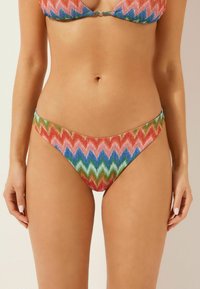 Bikini-set med ett livligt zickzackmönster i röd, blå, grön och rosa. Tyget har en texturerad yta med en glänsande finish. Design med minimal täckning.