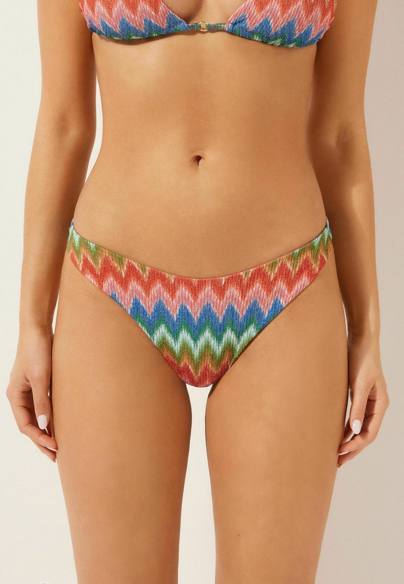 Bikini-set med ett livligt zickzackmönster i röd, blå, grön och rosa. Tyget har en texturerad yta med en glänsande finish. Design med minimal täckning.