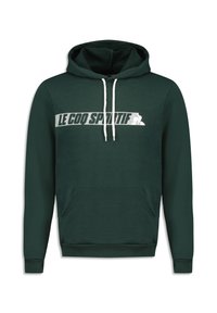 Sudadera verde oscuro hecha de una tela suave. Presenta un bolsillo frontal, cordones blancos y un logotipo blanco prominente en el pecho.