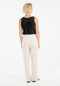 Top nero senza maniche con una finitura testurizzata e un retro plissettato, abbinato a pantaloni a gamba larga di colore crema e calzature nere slip-on.