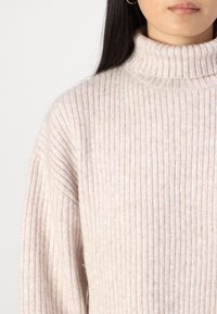 Hellrosa Rollkragenpullover mit geripptem Muster. Weicher Stoff und lockere Passform. Keine sichtbaren Muster oder Verzierungen.