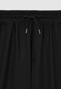 Pantaloni scurți negri plisati cu un talie elastică și un cordon de strângere. Țesătura are o textură canelată, care îi enhancează structura.