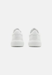 White leather sneakers featuring a rounded design, textured rubber sole, and embossed brand name on the heel. Smooth finish, minimal accents.