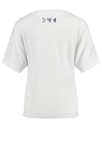 Camiseta blanca de manga corta con escote redondo y tres pequeños diseños de corazones negros en la espalda. Textura suave y lisa.