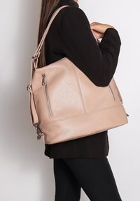 Una donna con indosso un blazer nero e pantaloni porta sulla spalla una grande borsa in pelle beige con tasche con zip.