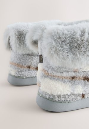 Harmaat pehmeät tohvelit, joissa on pörröinen resori ja raidallinen kuviointi kermaan, harmaaseen ja vaaleaan ruskeaan. Pohjassa näkyy sileä harmaa pohja.