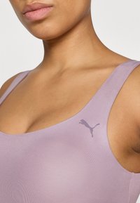 Un top sport de culoare mov deschis, realizat dintr-un material neted și elastic, cu decolteu rotund și un mic logo gri Puma pe partea stângă.