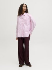 Light pink, long-sleeve shirt with a button front and single chest pocket, paired with wide burgundy trousers and brown shoes.