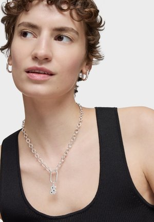 Collier en chaîne argentée avec un pendentif floral, comprenant des maillons et un fermoir. Porté sur un débardeur noir, mettant en valeur le design et les détails.