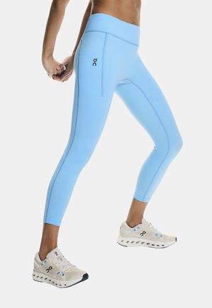 Person in hellblauen Leggings und weißen Laufschuhen, die die Arme hinter dem Rücken dehnt und in einer Ausfallschrittposition steht.