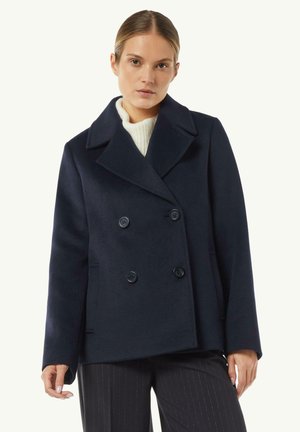 Marineblauer, doppelt geknöpfter Wollmantel mit großen Revers, zwei Vorderaschen und schwarzen Knöpfen, kombiniert mit einem cremefarbenen Strickpullover darunter.