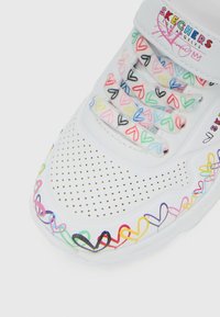 Sneaker bianca Skechers con motivi a cuore multicolori sui lacci, nella zona della punta e sul bordo della suola, caratterizzata da un design perforato nella parte anteriore.