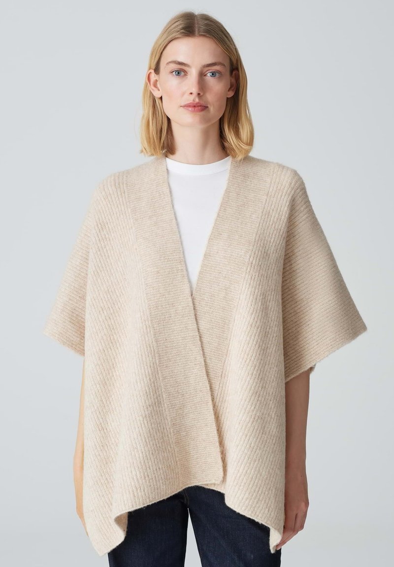 Poncho en tricot beige avec un motif rib élargi, devant ouvert et manches courtes, doté d'une coupe ample et d'un ourlet asymétrique.