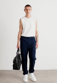 Camisa sin mangas blanca, pantalones con cinturilla elástica navy, bolso negro y zapatillas blancas. Tejido suave con un corte relajado, diseño minimalista.