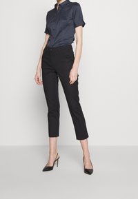 Marinblå knappad skjorta med uppvikt ärmar, i kombination med svarta åtsittande byxor och svarta stilettklackar. Slät tyg och skräddarsydd passform.