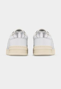 Ζευγάρι λευκών αθλητικών παπουτσιών με ασημένιες λεπτομέρειες στη φτέρνα, εμφανιζόμενα από πίσω σε απλό λευκό φόντο.